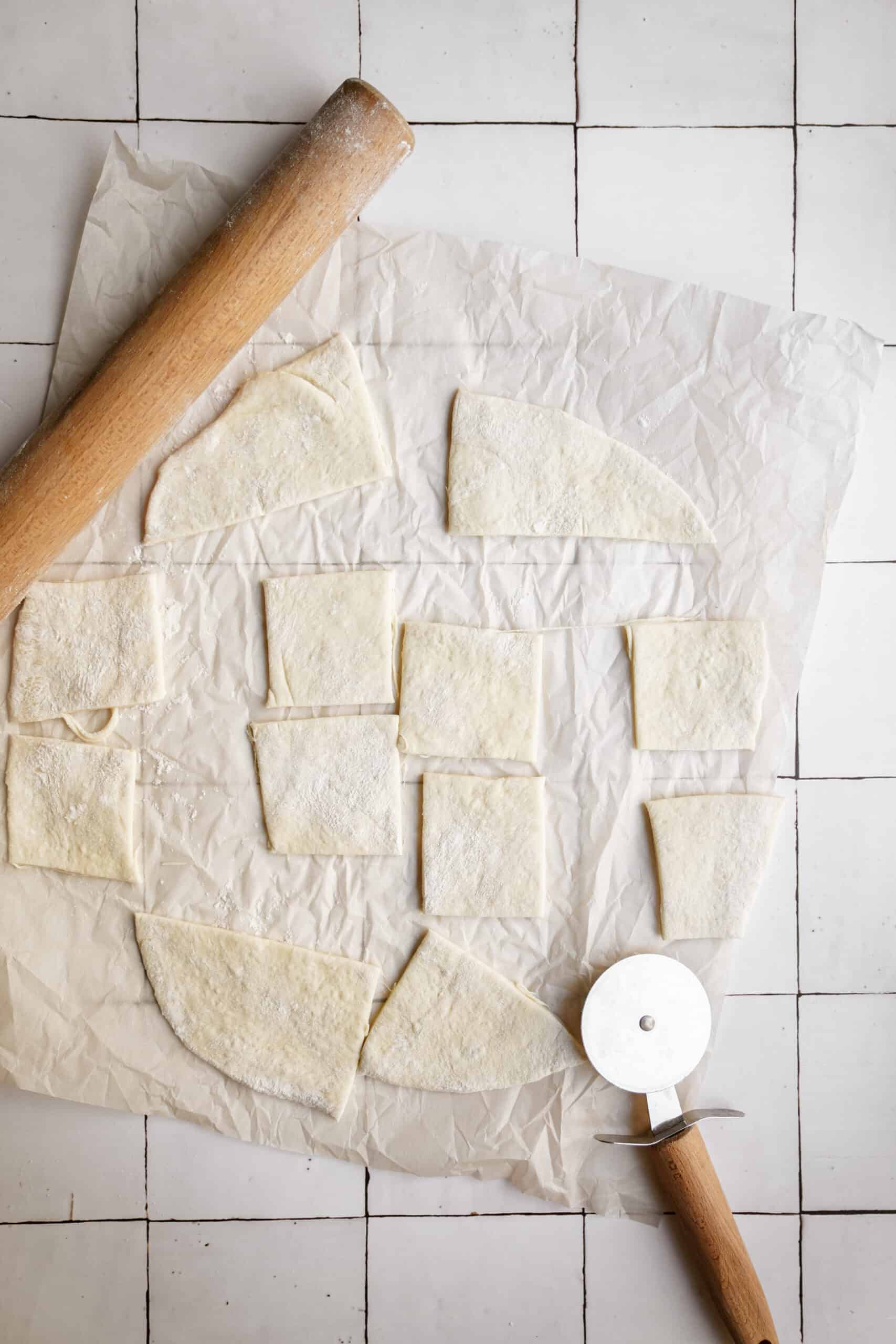 Pizza dough being rolled and cut on parchment 