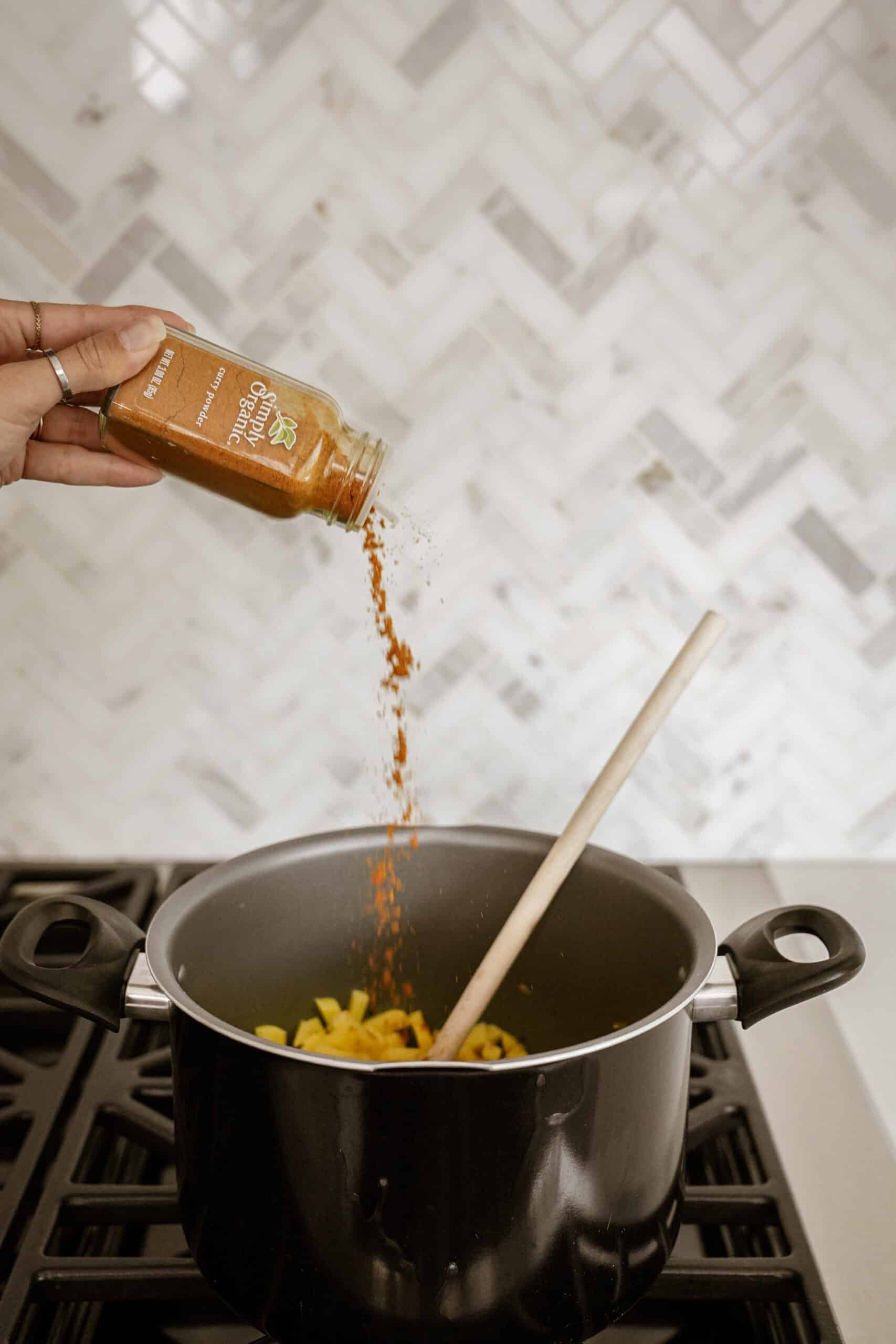 Curry powder being poured into a pot with raw potatoes