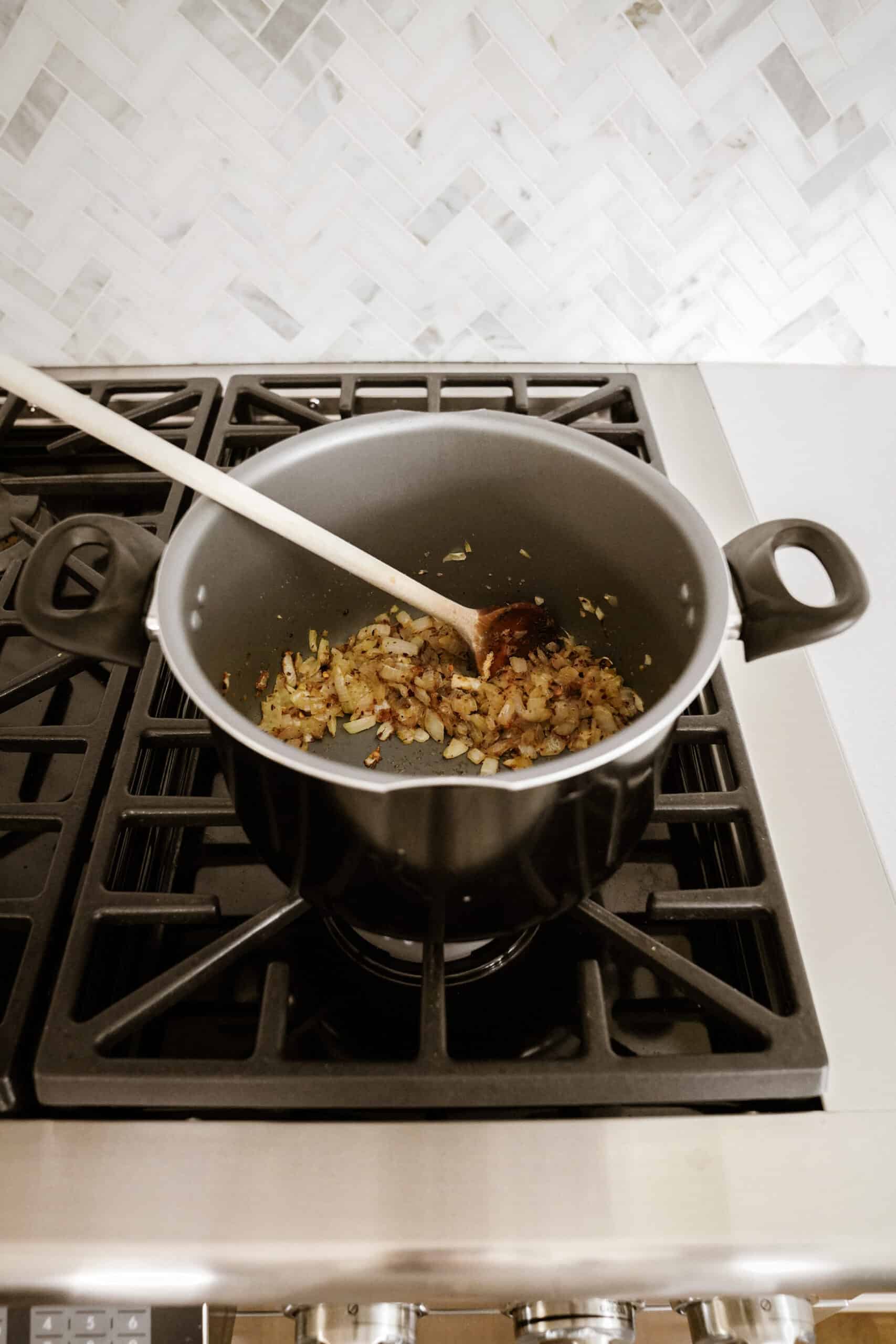 Onions in a pot on a stove with a wooden spoon