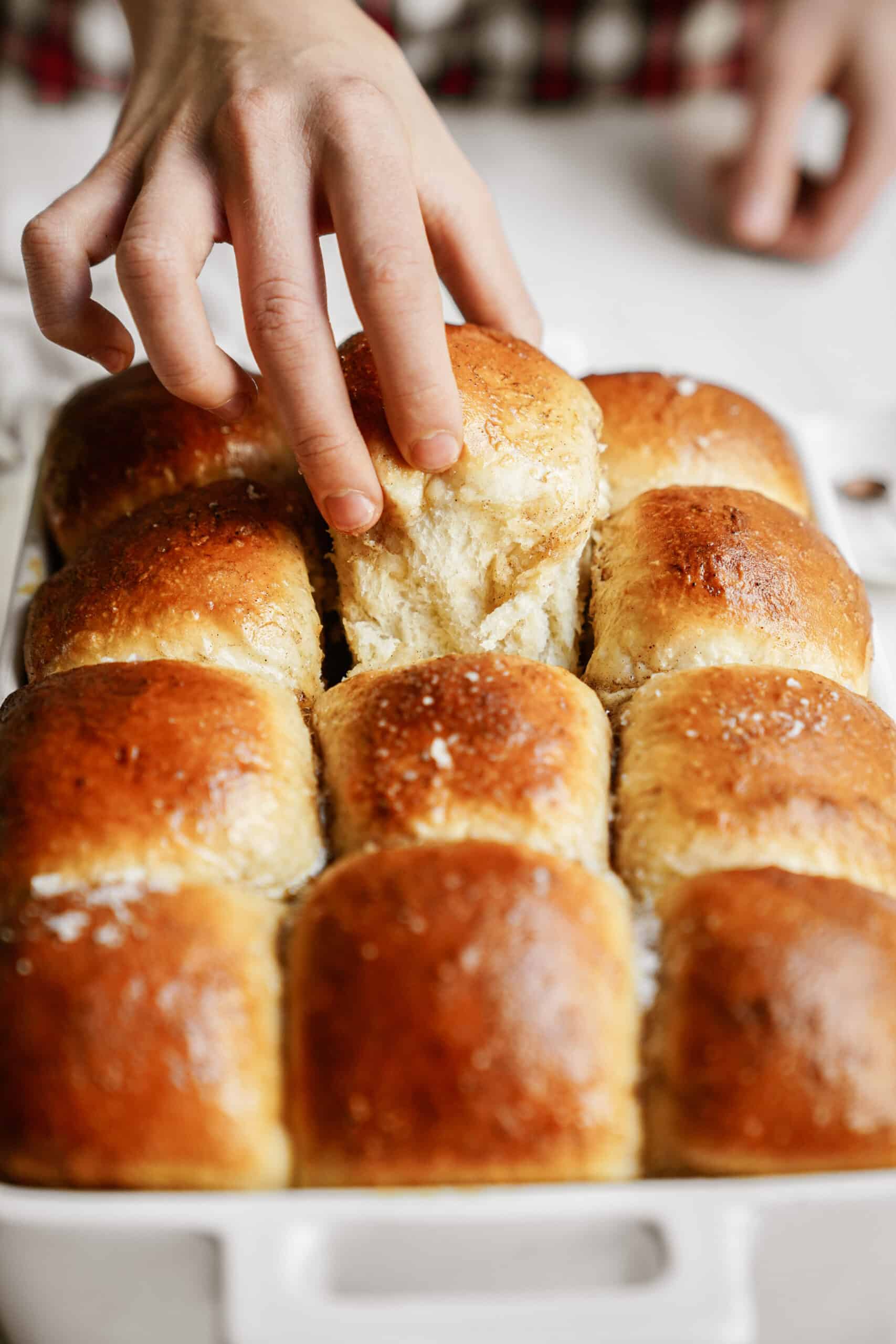 Hand taking easy dinner roll out of casserole dish