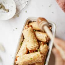 Baked brie bites in a mini white dish with honey being drizzled on