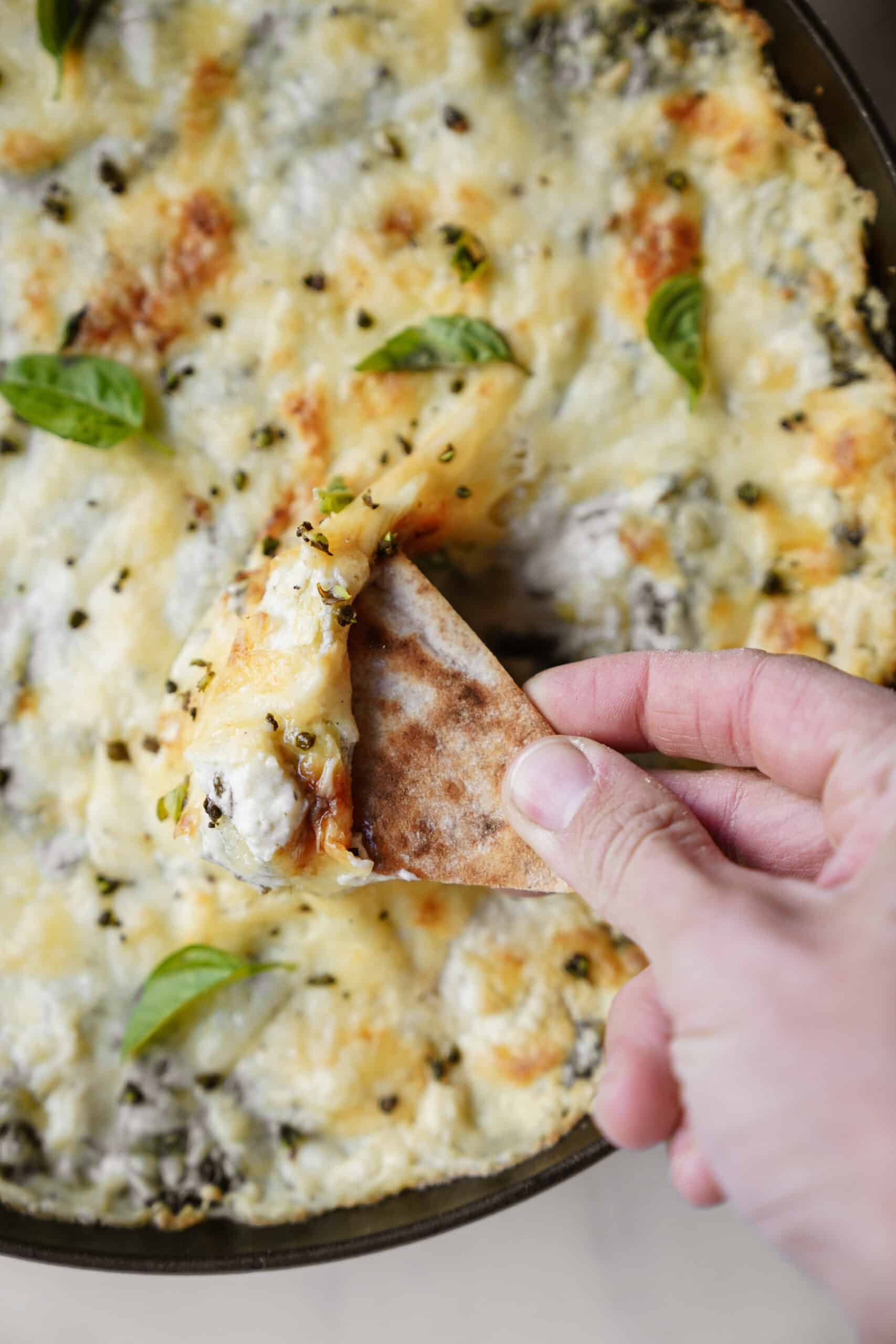 Spinach and Artichoke Dip in cast iron dish with hand dipping pita chip in