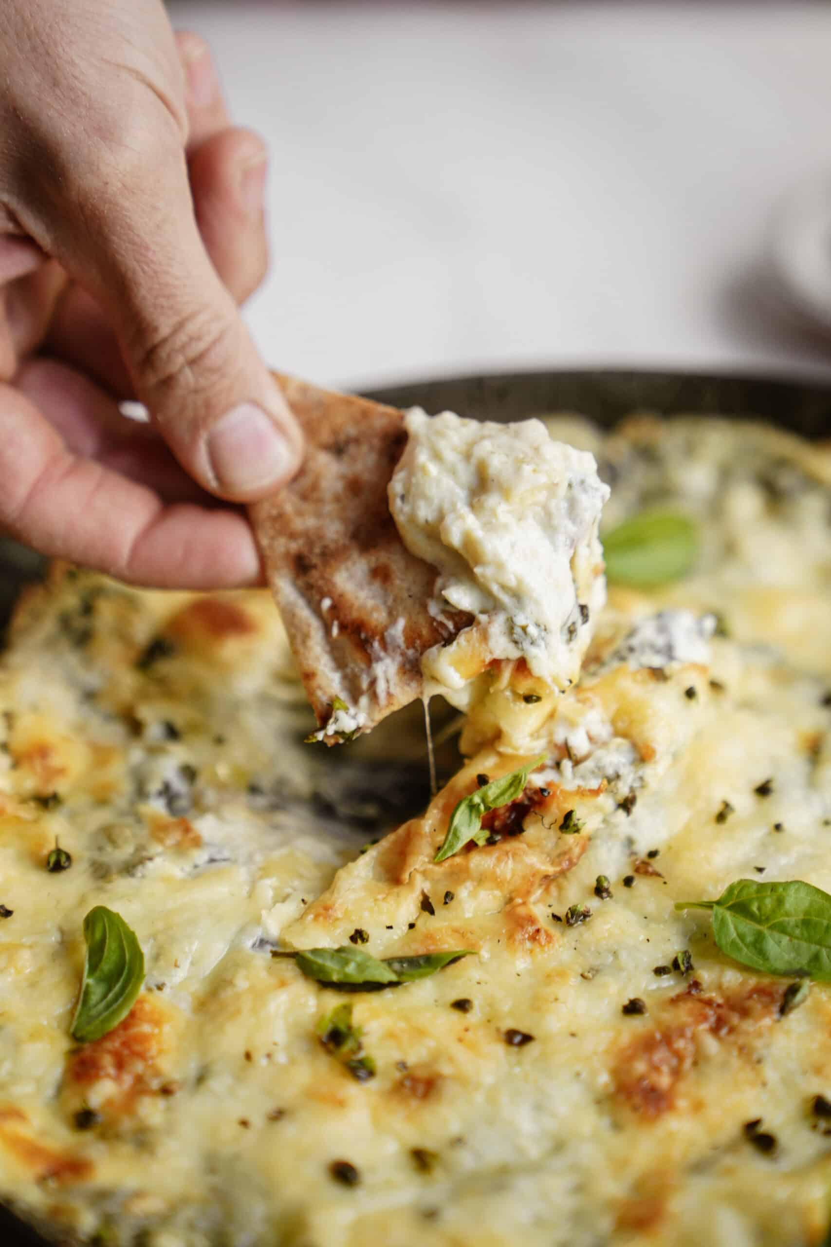 Spinach and Artichoke Dip in cast iron dish with hand dipping pita chip in