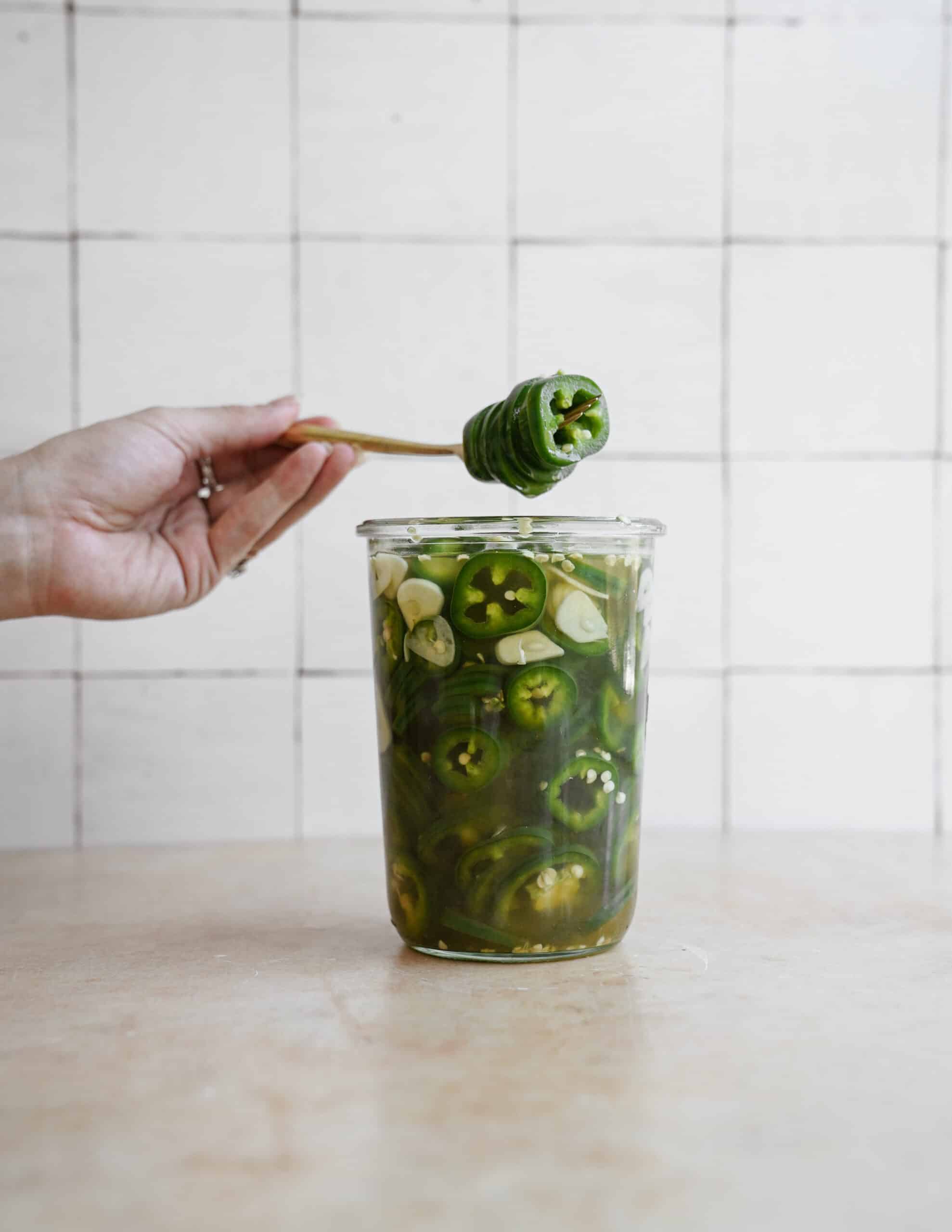 Fork picking pickled jalapenos out of a mason jar