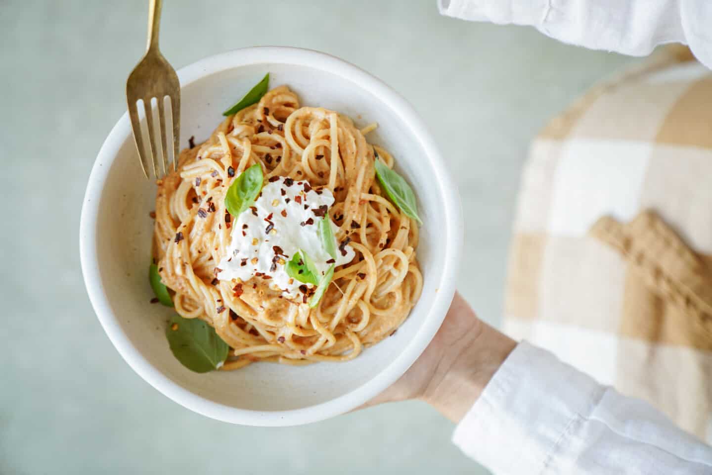 Hands holding a bowl of burrata pasta