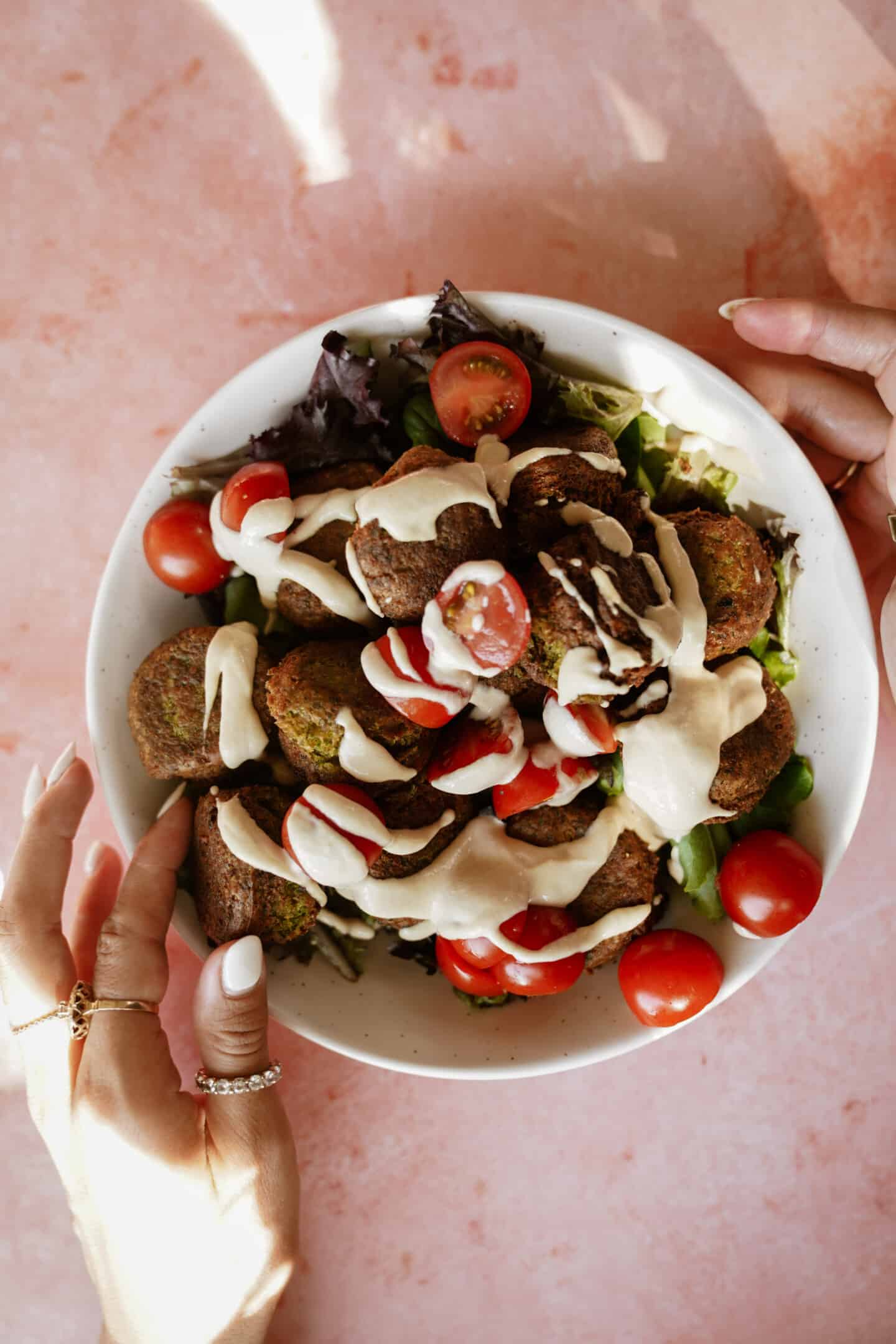 Fresh salad greens and tomatoes with falafel on top and drizzled with tahini sauce