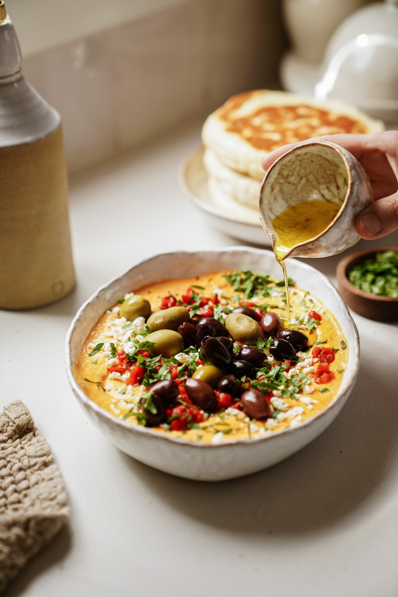 A bowl of spicy feta dip with olive oil being drizzled on top