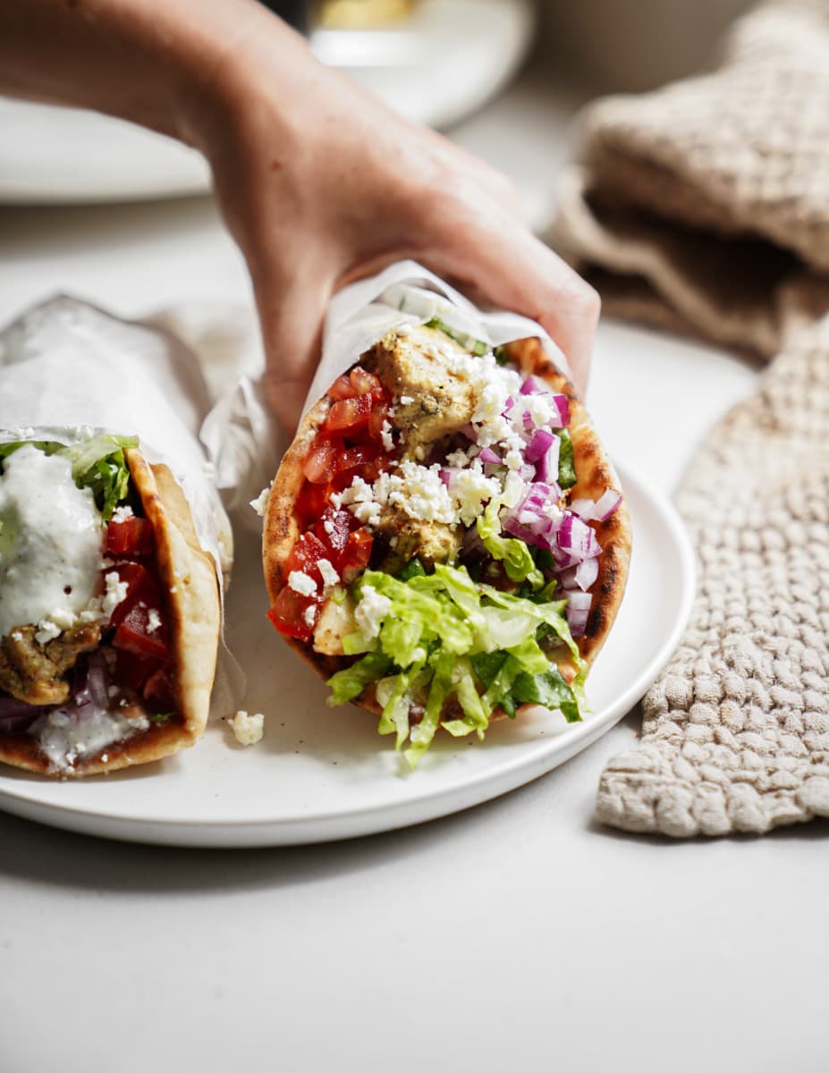 Chicken gyros on a plate with a hand reaching for the wrap