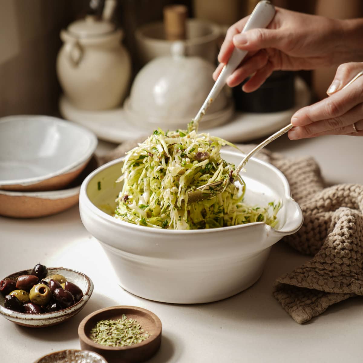 Hands scooping out greek cabbage salad with serving spoons