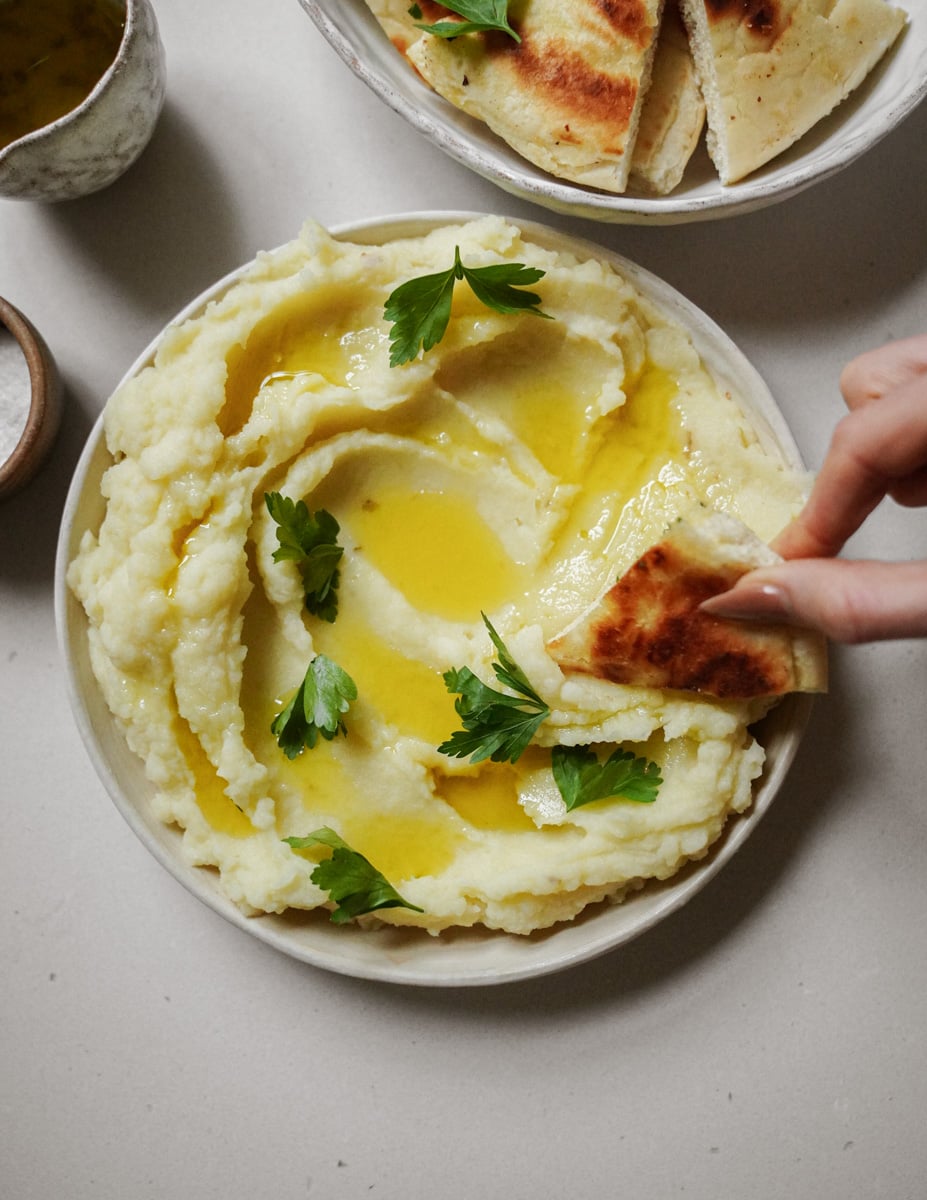 Skordalia in a bowl with bread dipping into it 