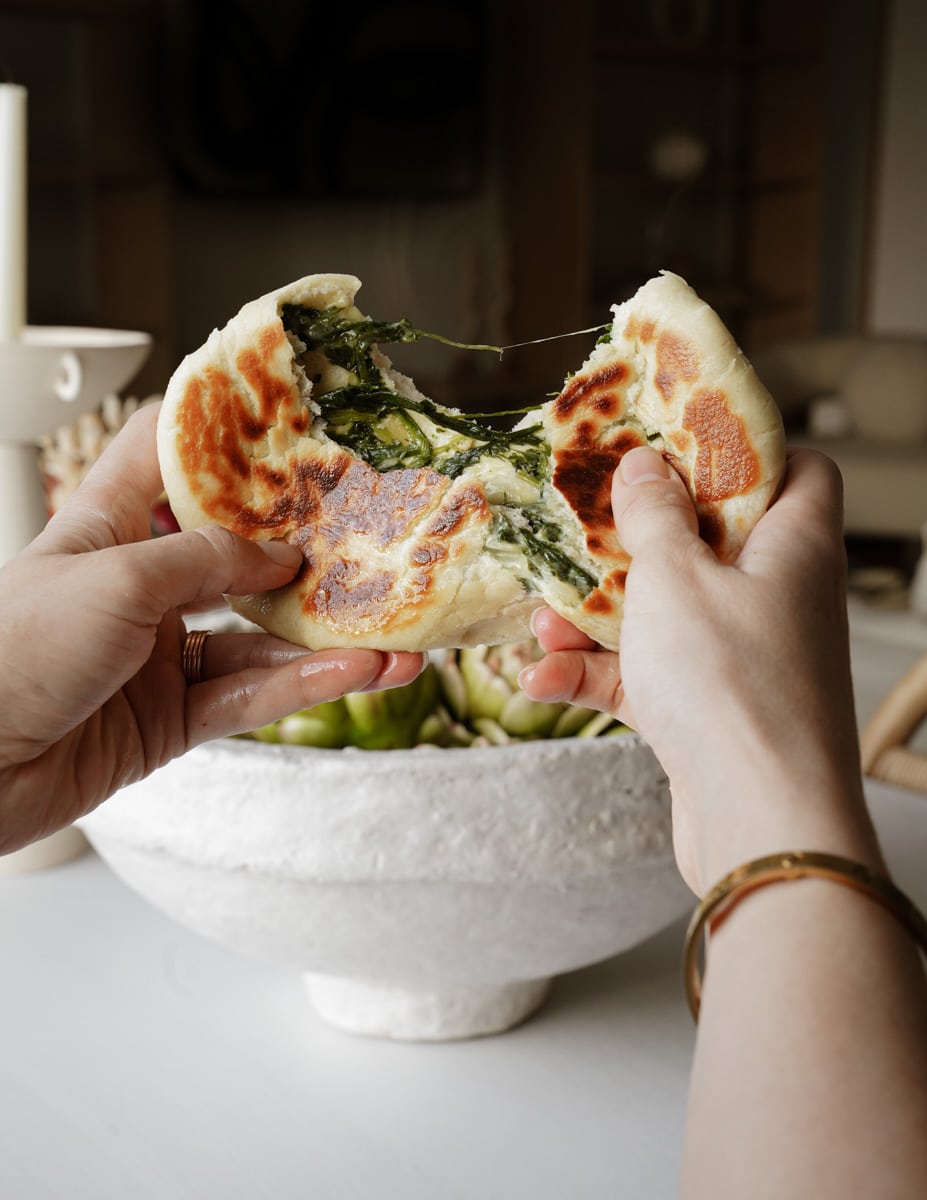 Hand pulling a part a fluffy pita with spinach in it 