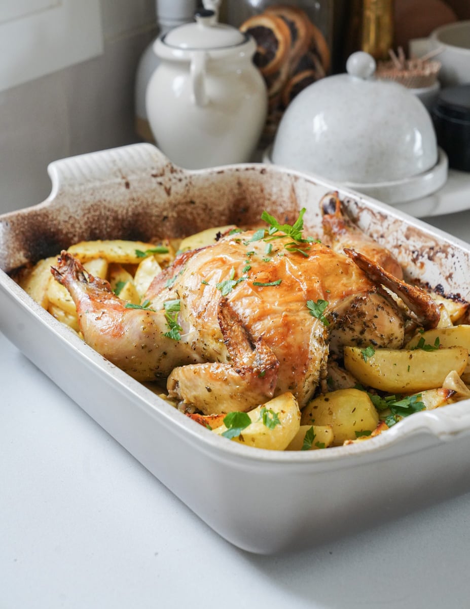 Whole roasted chicken in a casserole dish with potatoes