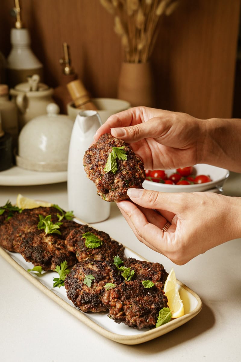 Greek Burger on a plater with hands holding a patty