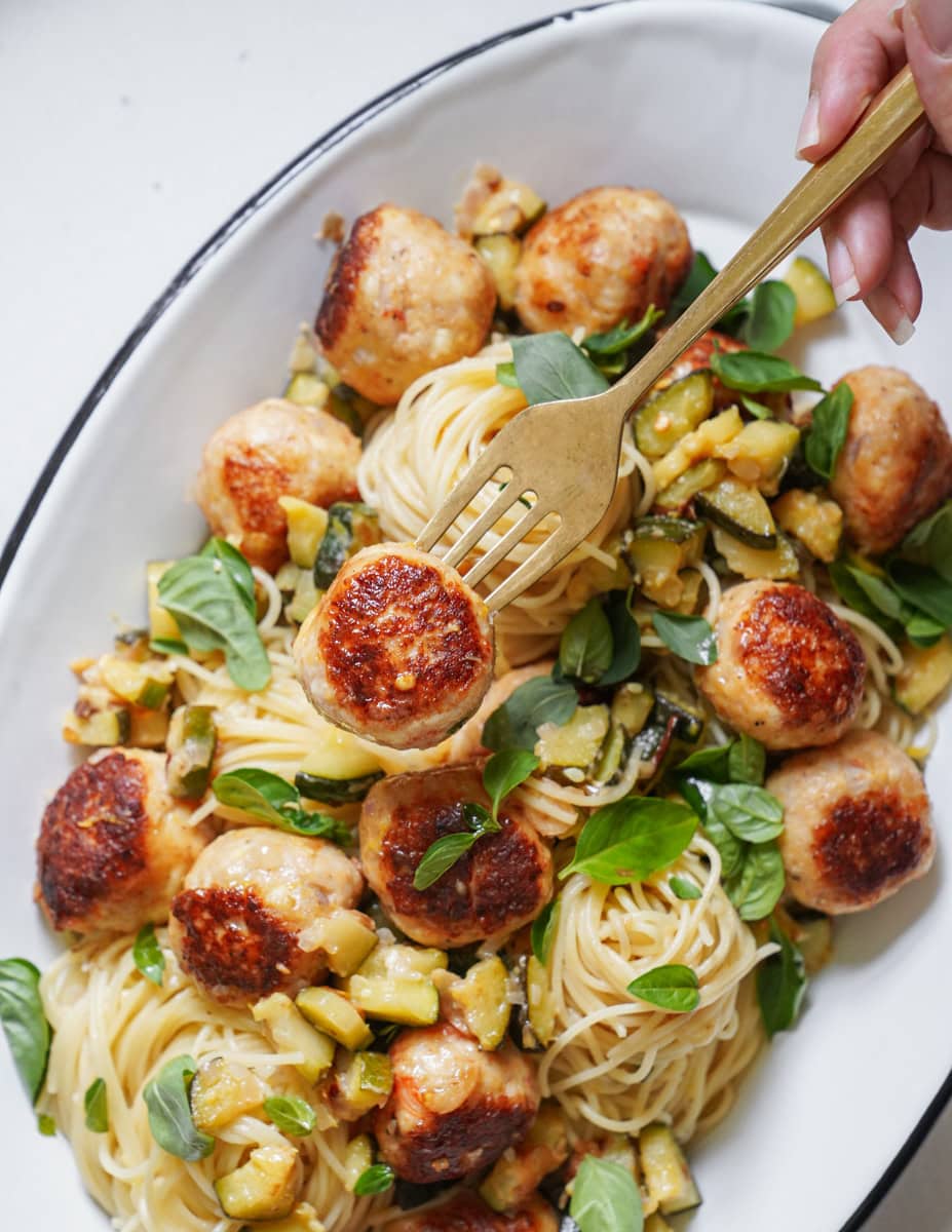 A fork digging into angel hair pasta with shrimp balls