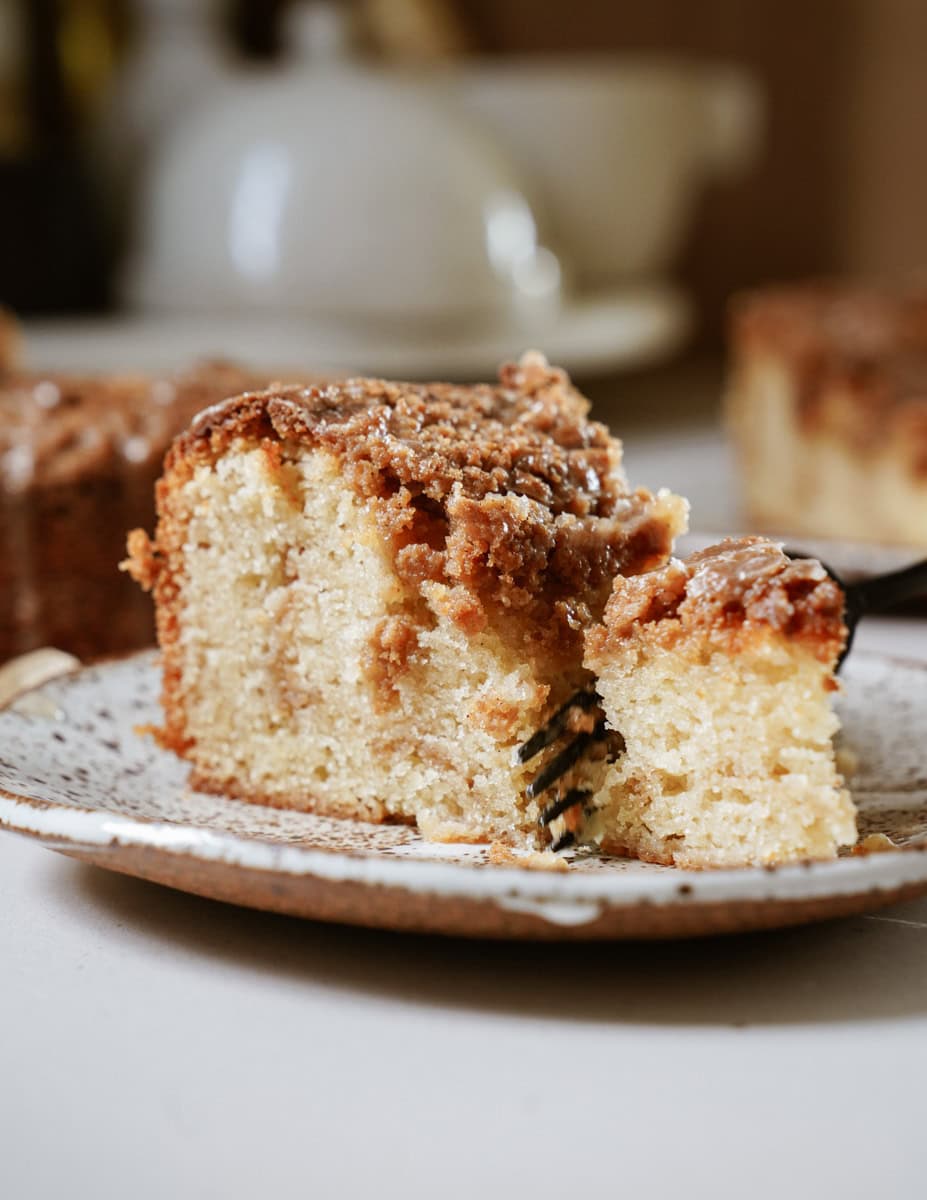 A slice of golden-brown coffee cake topped with a generous layer of cinnamon-sugar streusel, on a white plate.