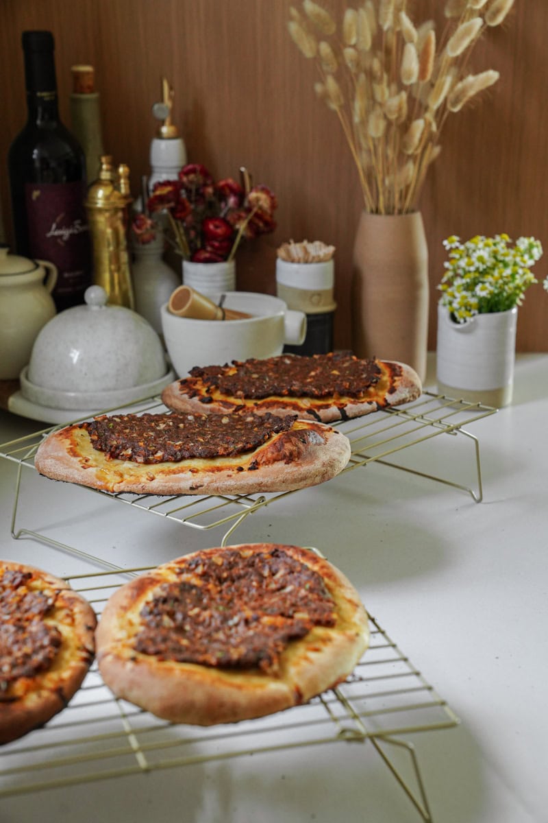 Four golden-brown Manakeesh flatbreads topped with ground beef and arranged on a metal cooling rack.