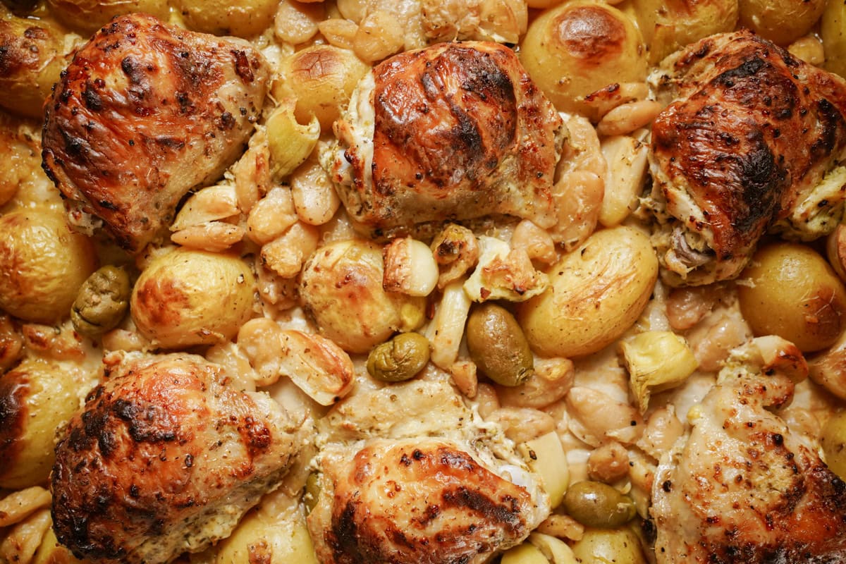 A sheet pan of deliciously cooked marinated chicken with roasted potatoes, garlic and green olives. 