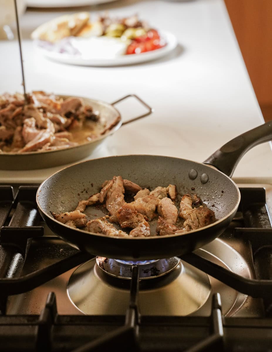 Seasoned gyro meat sizzles in a hot pan, its edges turning golden-brown and crispy.