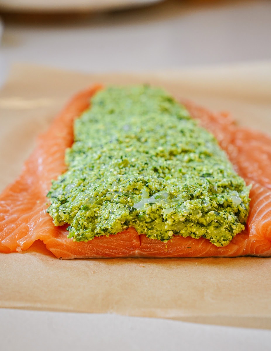 An uncooked salmon fillet is partially opened, revealing a vibrant green stuffing of spinach, feta, and shrimp